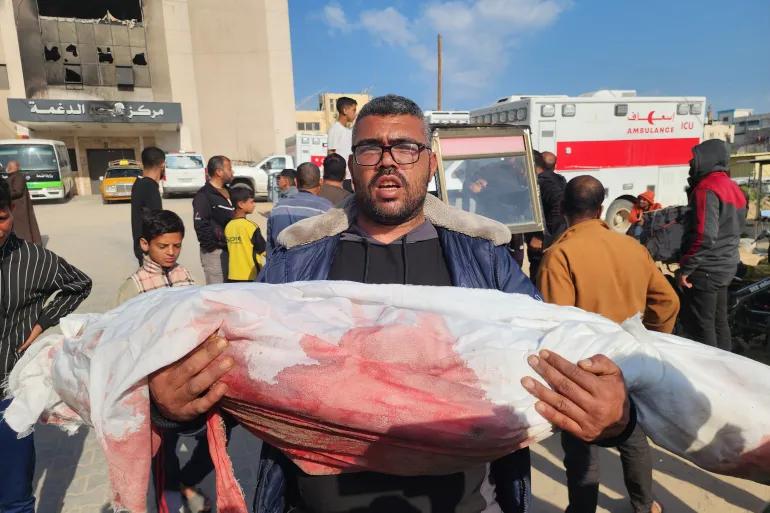 A mourner carrying the bloodstained,covered body of a child from Khan Younis Gaza’s Nasser Medical Complex morgue, on March 18, 2025. Image: Hani Alshaer