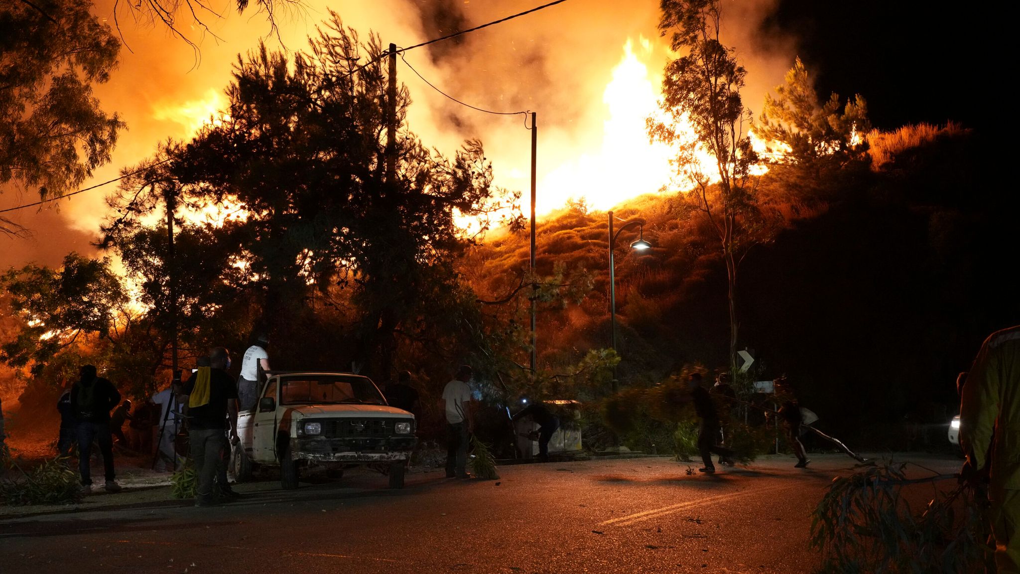 Thick smoke fills the sky as onlookers anxiously watch the fire edge closer to residential areas. [Politischios.gr /AP via SkyNews]