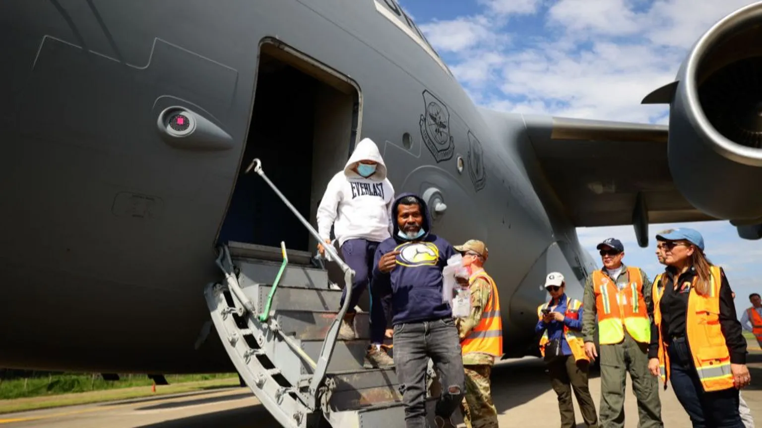 This image depicts migrants deported by the US arriving in Honduras in January 2025. They disembark a US Air Force plane and are met by officials who provide assistance as part of deportation agreements between the two countries.