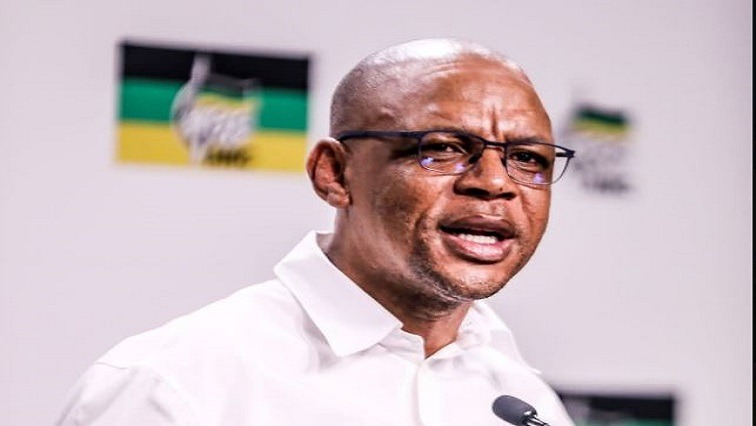 Image Credit: X @Pule Mabe Pule Mabe, wearing glasses and a white shirt is speaking into a microphone, with a backdrop displaying the ANC (African National Congress) logo in green, yellow, and black colors.