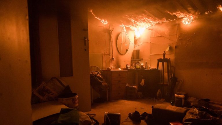 Residential Fire Incidents showing a room engulfed in flames, with fire spreading across the ceiling and an intense orange glow illuminating the entire room, highlighting the urgency and danger of the scene.