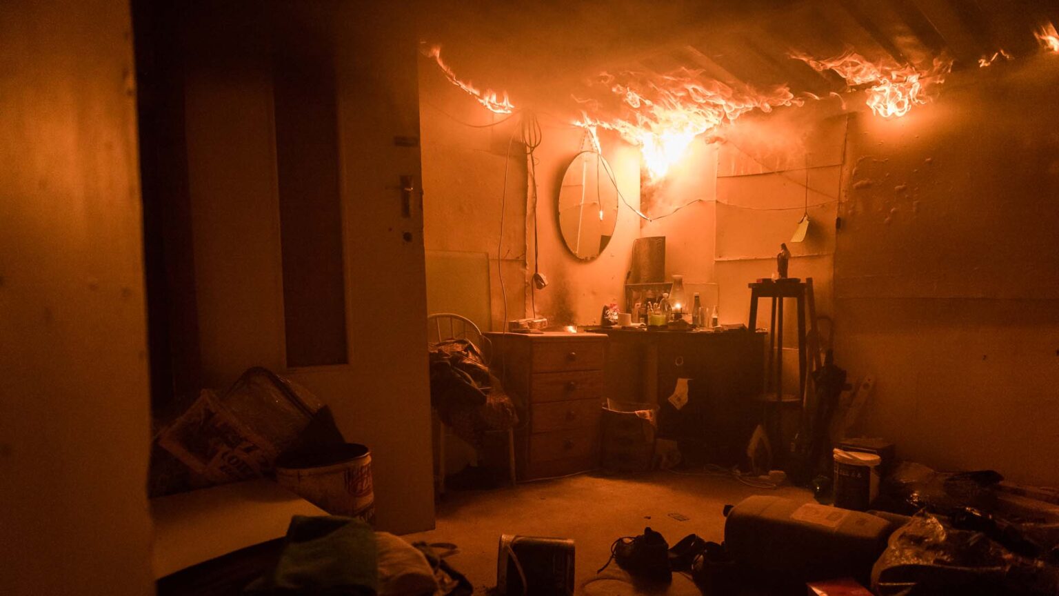 Residential Fire Incidents showing a room engulfed in flames, with fire spreading across the ceiling and an intense orange glow illuminating the entire room, highlighting the urgency and danger of the scene.
