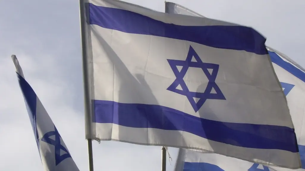 Israeli flags wave against a cloudy sky.