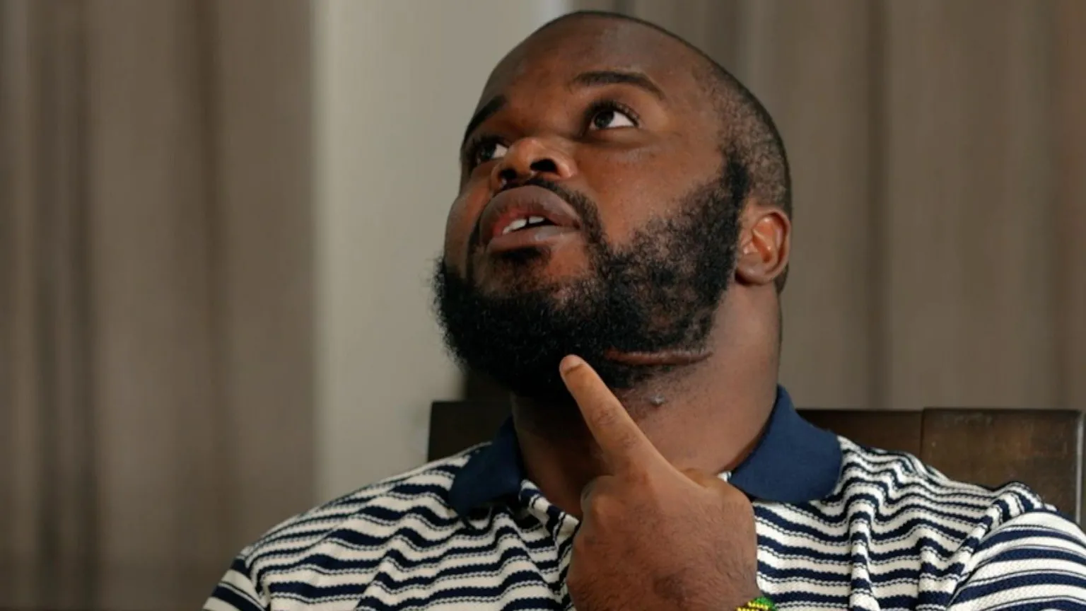 Tanzanian activist Edgar Mwakabela, known as Sativa, pointing to his jaw while seated indoors, reflecting on his escape from abduction.