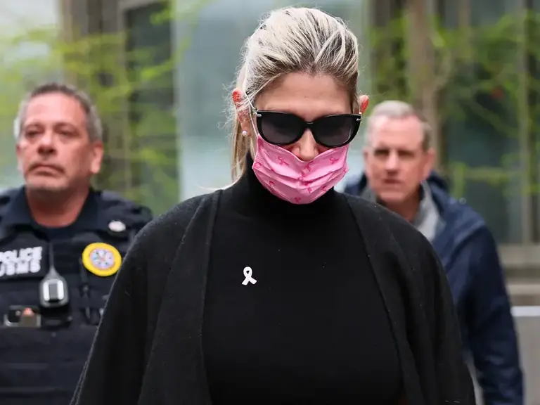 Former Senator's Spouse Nadine Menendez wears a pink breast cancer awareness mask and dark sunglasses while walking outdoors, flanked by law enforcement officers.