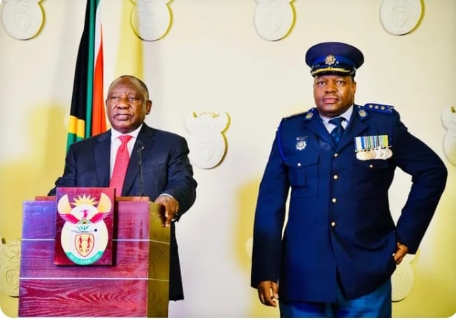 Ramaphosa 121 KZN killing dockets — President Cyril Ramaphosa stands at a podium with the South African coat of arms, delivering a speech beside National Police Commissioner General Fannie Masemola, who is in full blue uniform with medals, in front of a backdrop featuring the national flag and emblem.