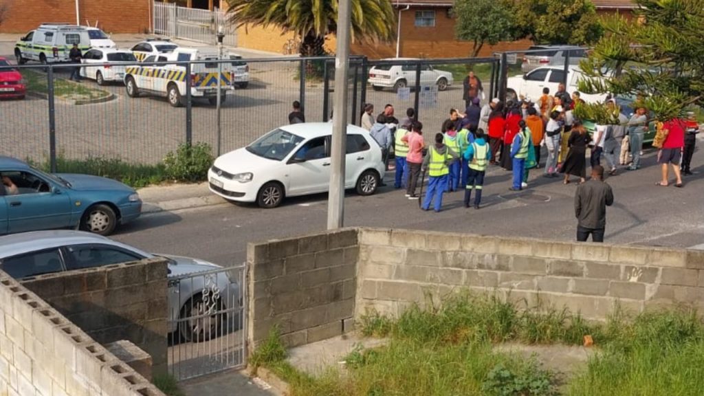 Mitchell's Plain school gates surrounded by concerned parents, learners, and security personnel after false reports of armed individuals caused panic.