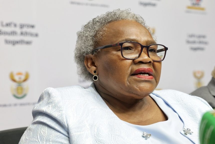 Sassa ends Postbank deal as Social Development Minister Nokuzola Tolashe speaks at a press conference wearing a light blue outfit and glasses.