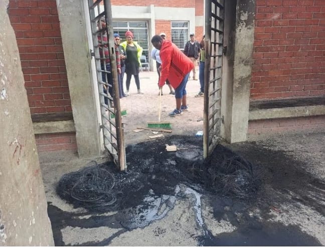 A person sweeps debris and burnt material at the entrance gate of a damaged clinic in Khayelitsha’s Town Two after a protest.