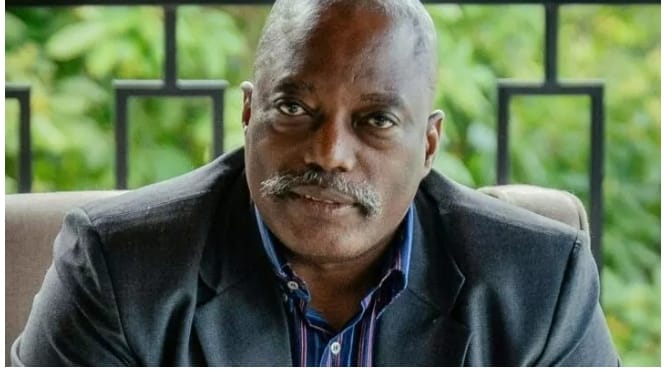 Kabila sitting in a chair, wearing a dark suit jacket and striped shirt, looking directly at the camera with a serious expression.